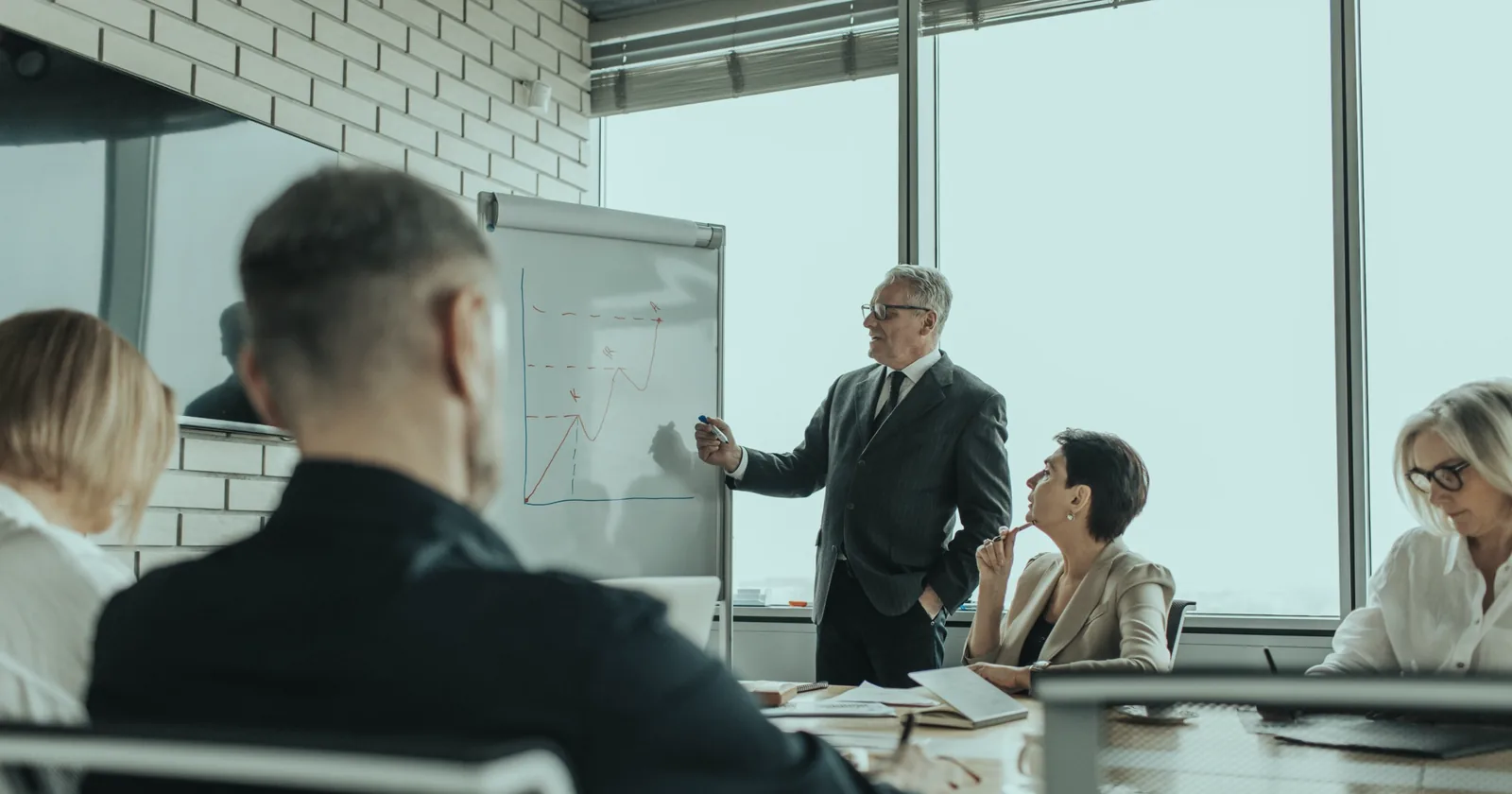 A senior colleague presenting a performance chart on a flipchart to a team in a meeting room